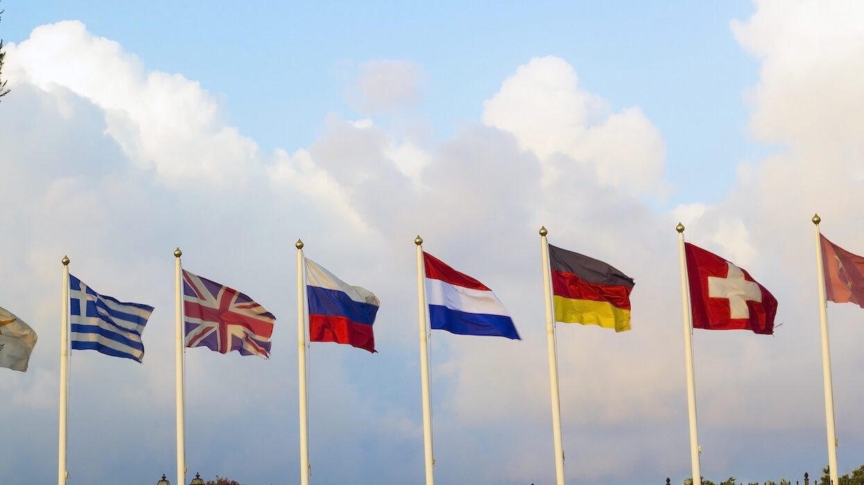 Flags Of Different Countries Flapping In Wind Against Blue Sky, iStock